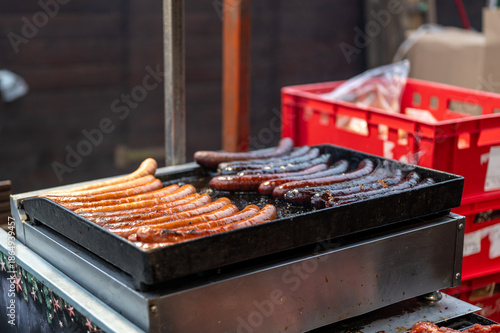 Close up view of grill at christmas market stall with sausages and meat cooking over hot coals, street food scene with smoke, heat and traditional winter festive atmosphere