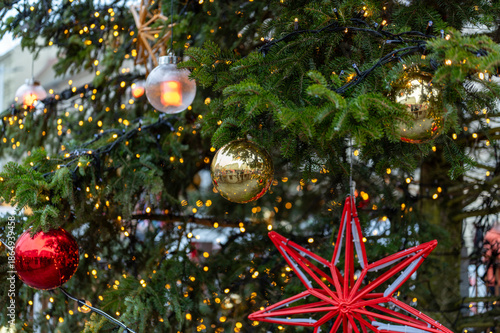 Close up detail of christmas tree decorations with red and gold baubles, star shaped ornaments and warm lights imitating fire, festive holiday atmosphere in brno city