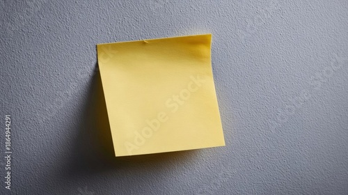 Close-up of a single yellow sticky note pinned to a gray wall. the note is rectangular in shape and appears to be made of paper or a similar material.
