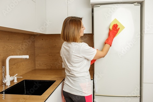 Young woman cleaning kitchen fridge with gloves