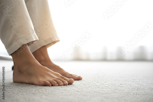 A man's feet are bare on a carpeted floor. Concept of relaxation and comfort, as the man is barefoot and standing in a room with a white background. The bare feet suggest a casual