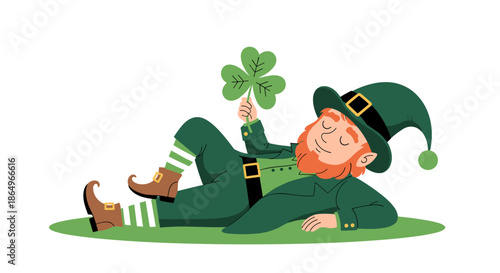 Happy leprechaun with a ginger beard sleeps on the green grass while holding a lucky four-leaf clover in his hand.