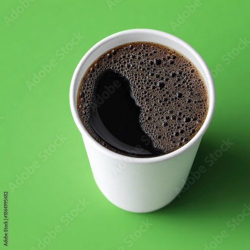 Coffee in a plain white cup, dark liquid with bubbles on a green surface