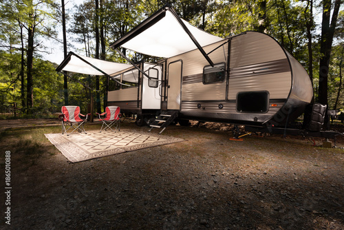 Awnings out on a travel trailer set up for camping at a daytime campsite surrounded by trees.