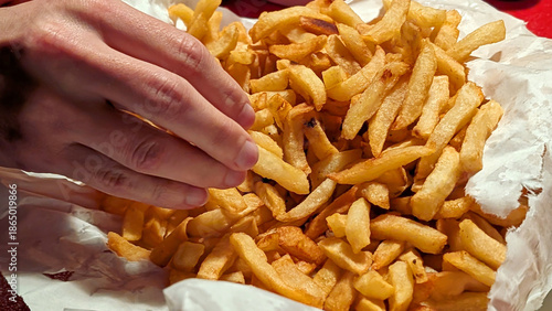 A close up of a Hand takes delicious fresh Authentic Belgian Frites from paper container at table. Local flavor concept.