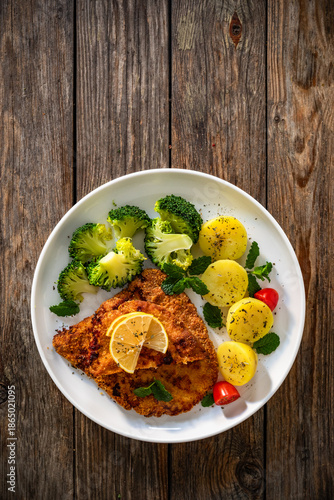 Crispy air fryer breaded pork chop with broccoli and boiled potatoes on wooden table. Top view	