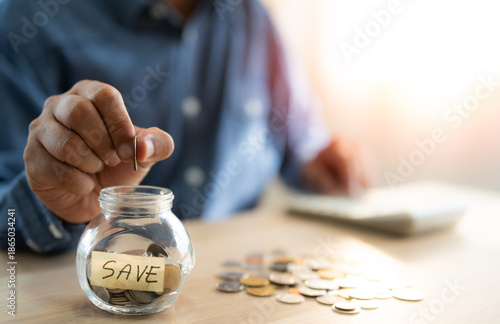 A man hand putting coins into glass bottle saving bank for account save money. Planning step up, saving money for future plan, retirement fund. A business investment-finance accounting concept.