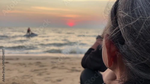 Unidentified elderly woman looking out to sunset at beach Pattaya.