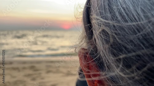 Unidentified elderly woman looking out to sunset at beach Pattaya.