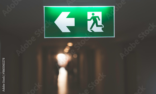 Green emergency exit sign with running man icon and arrow inside modern building corridor representing safety of evacuation route for fire escape, emergency exit, security signage and public safety.