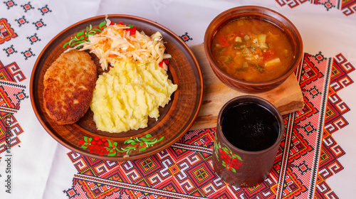 Traditional Ukrainian lunch with mashed potatoes, meat cutlet, vegetable soup and kvass on embroidered tablecloth