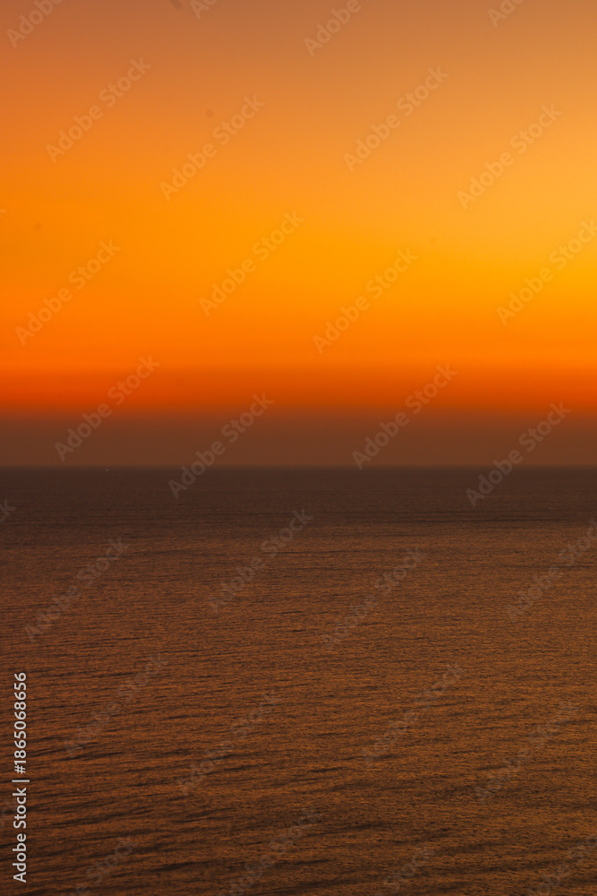 Naklejka premium Minimalist ocean sunset with a smooth orange and blue sky gradient above calm sea water, creating a peaceful abstract seascape ideal for background, meditation, nature, and atmospheric design concepts