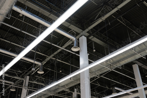 Industrial ceiling with exposed ventilation ducts, metal beams, and linear LED lighting inside a modern commercial or industrial building.