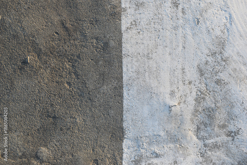 Concrete wall texture with a faded vertical white paint stripe. Minimal cement surface featuring contrasting painted and raw sections. Abstract concrete wall with vertical division and natural wear.