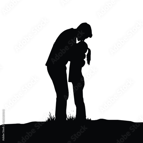 Silhouette of a loving father gently kissing his young daughter's forehead outdoors near the ground