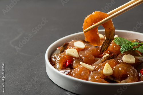 Korean style soy marinated shrimp being picked with chopsticks, glossy sauce dripping in a white bowl. Popular Korean seafood dish known as saeu jang, premium raw shrimp