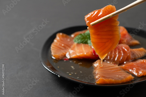 orean soy marinated salmon slices being picked with chopsticks, sauce dripping on black plate. Popular Korean food known as salmon jang, premium seafood