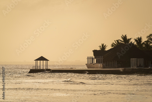Serene sunset view of a tranquil waterfront boardwalk with lounge chairs, offering a peaceful escape.Monochrome orange photo, Dominican republic.
