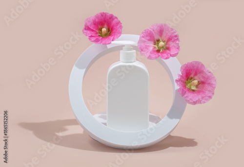  white cosmetic bottle with pink hollyhock flowers in a modern round frame on a pastel background