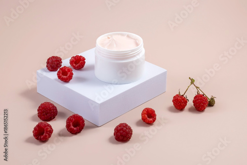 jar of hand or face cream and raspberries on a stone podium on a pink background