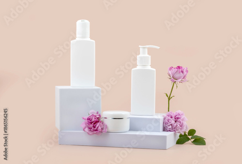 containers for skin care products on a white podium and rose flowers on a beige background