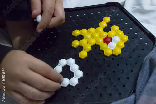 Close-up of child's hands playing with hexagonal mosaic puzzle on a black board.