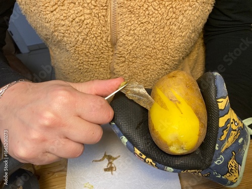 Wallpaper Mural Hände schälen eine Kartoffel mit Messer über einer Schüssel in der Küche. Das Motiv steht für Kochen, Hausarbeit, Vorbereitung von Mahlzeiten und alltägliche Küchenroutine. Torontodigital.ca