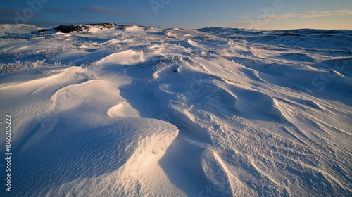 Wind sculpted snow drifts forming abstract patterns across a cold frozen landscape under a clear blue sky during golden hour