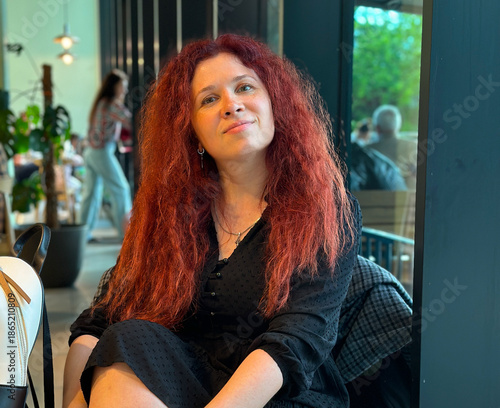 Woman sitting in cafe interior and looking at camera. Relaxed lifestyle portrait, casual meeting, urban leisure and calm social atmosphere
