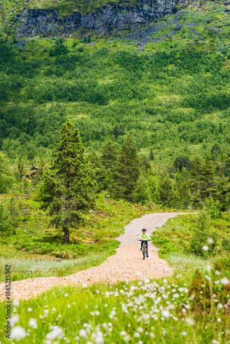 Boy rides mountain bike on dirt path in Norway surrounded by greenery and hills during daytime
