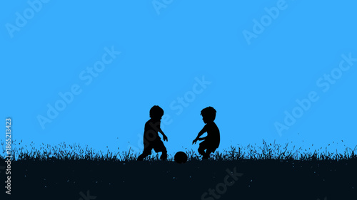 Two young children playing football on a grassy field silhouette against a clear blue sky, depicting childhood fun and outdoor activity.