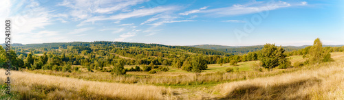Rural summer landscape panorama of the Góry Sowie (Owl Mountains), Poland, featuring rolling green hills, open meadows, dense forests, scattered farms, country roads, and a clear blue sky.