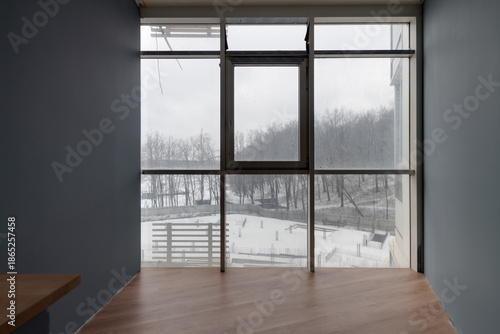 Empty apartment interior with large panoramic window overlooking winter construction site