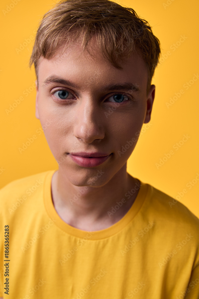 Fototapeta premium Closeup of a young boy wearing a yellow shirt against a warm yellow background, calm expression, soft studio lighting, clear eyes and smooth skin with natural details