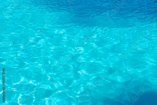 Clear turquoise water ripples in a swimming pool. Sunlight creates a beautiful shimmering pattern. A perfect background for summer vacation.