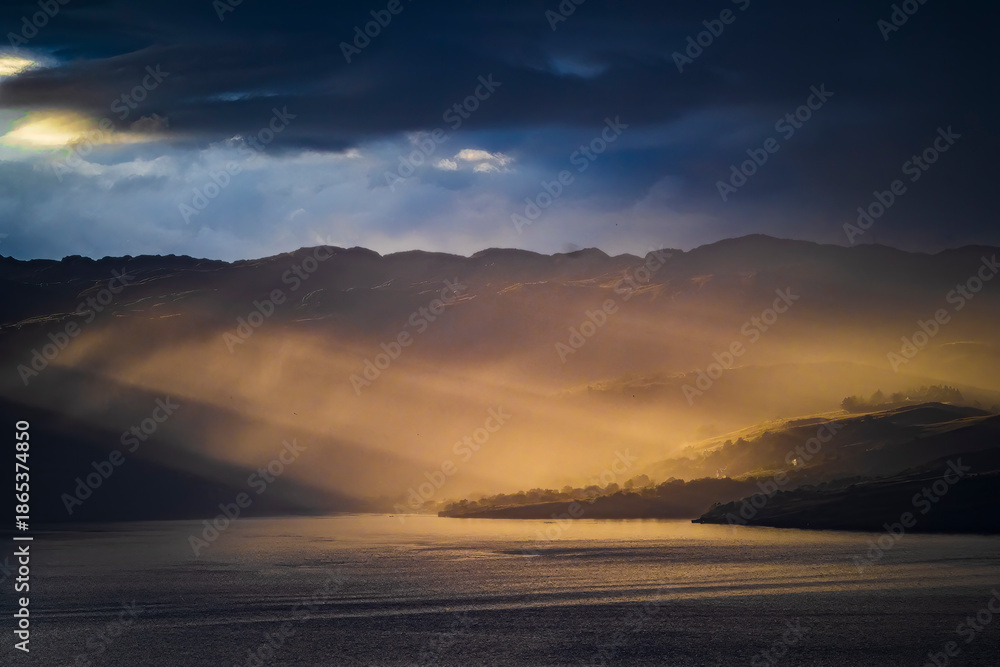 Fototapeta premium Sunbeams breaking through clouds over Scottish loch