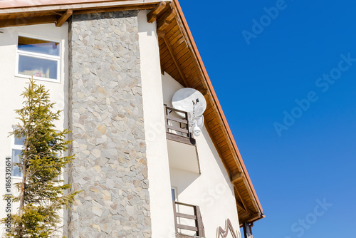 Modern private villa house with parabolic satellite dish antennas.Real estate property.Wireless television broadcasting receiver on wall,open balcony,bright blue sky.