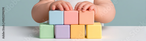 Soft pastel colored wooden blocks stacked by child hands on white table with blue background, playful and educational toy for early development and learning