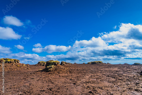 Eroded peatland landscape with exposed dark soil and isolated peat ‘islands’ under a bright blue sky