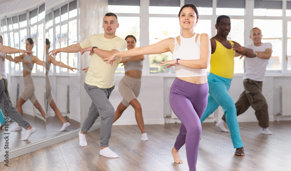 Obraz premium Sporty smiling young Asian woman practicing rhythmic aerobics during group workout in fitness studio. Active lifestyle concept