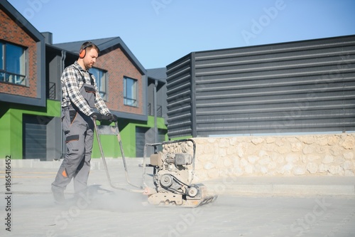 Fotografia Landscaping worker using vibratory tamping machine plate compactor on a new pati