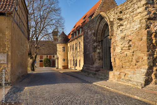 Mittelalterliches Steinportal mit Holztür und Blick auf die historische Klosteranlage im Sonnenlicht, Memleben, Burgenlandkreis, Sachsen-Anhalt, Deutschland