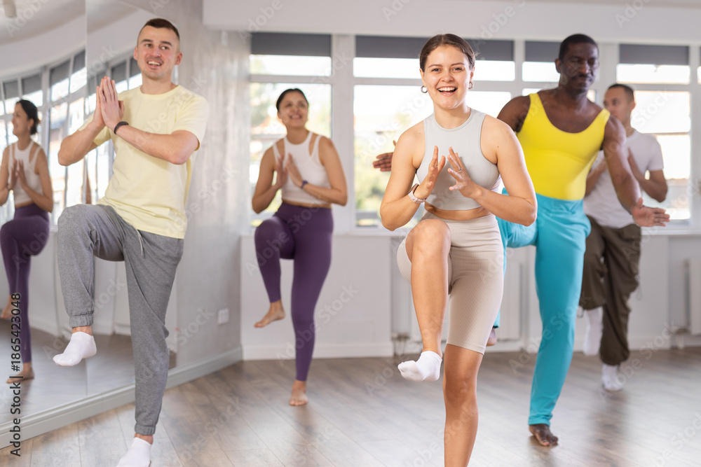Fototapeta premium Enthusiastic young fit girl in casual activewear with captivating smile energizing group during dance fitness class in well-lit mirrored studio..