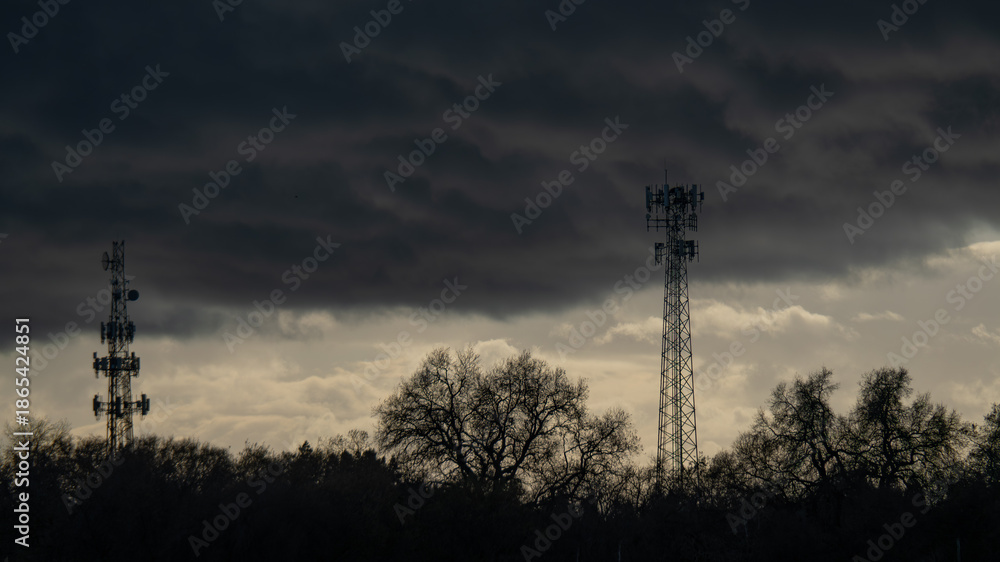 Fototapeta premium Industrial cell towers stand tall against a gathering winter storm