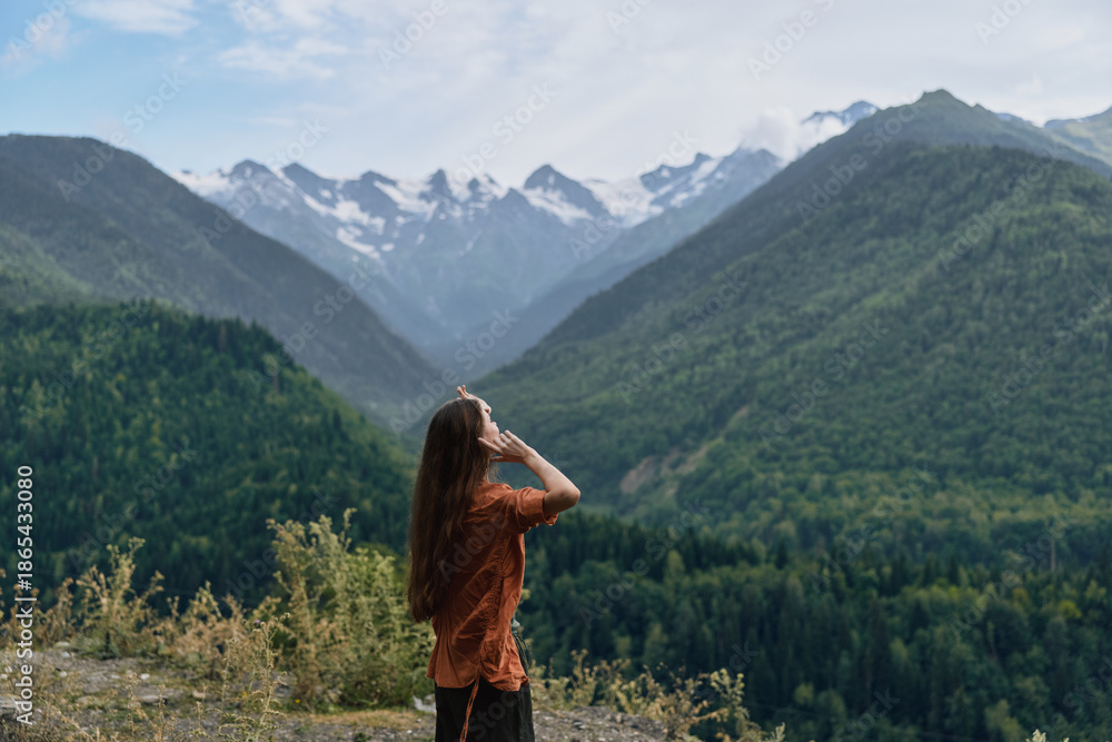 Naklejka premium A woman stands on a hillside gazing at snow capped mountains in a lush valley, capturing a tranquil outdoor landscape and wide open nature