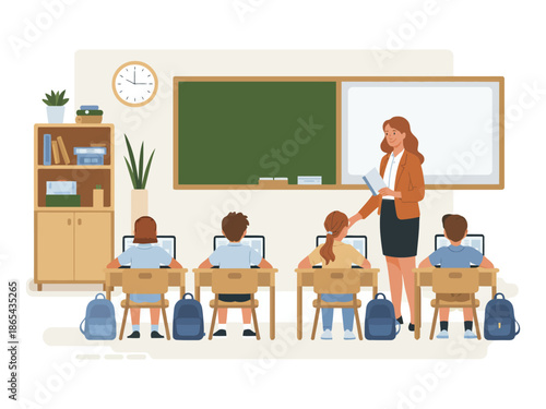 A teacher standing in a classroom with students sitting at desks using laptops