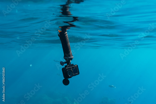 Action camera on a floating hand grip handle underwater in clear blue sea water with small fish on the background