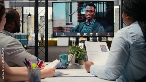 Recruiters team and male candidate engage in a video call discussion with webcam and high tech tools, reviewing the resume and job search progress during a remote interview conference. Camera A.