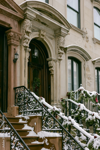 Snow covers steps and railings of a brownstone house during winter in a quiet neighborhood in December