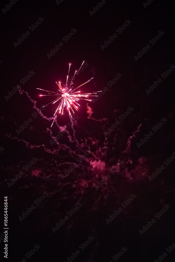 Fototapeta premium Pink fireworks exploding in night sky with smoke trails, dramatic celebration scene